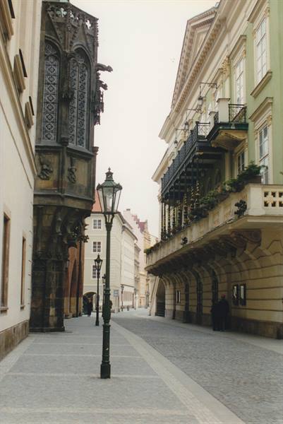 Gothic stone oriel bay window beside a neoclassical building with wrought-iron balcony
