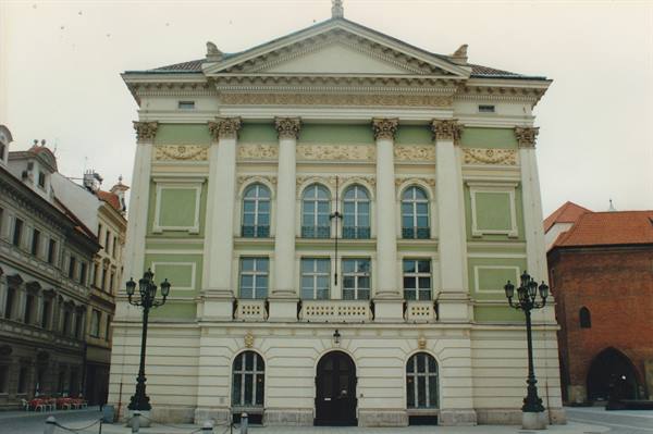 Green and white neoclassical facade with columns and pediment, cast-iron lanterns on the square