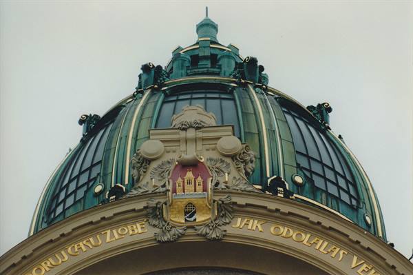 Green copper dome of Prague's Municipal House with golden crest and inscriptions