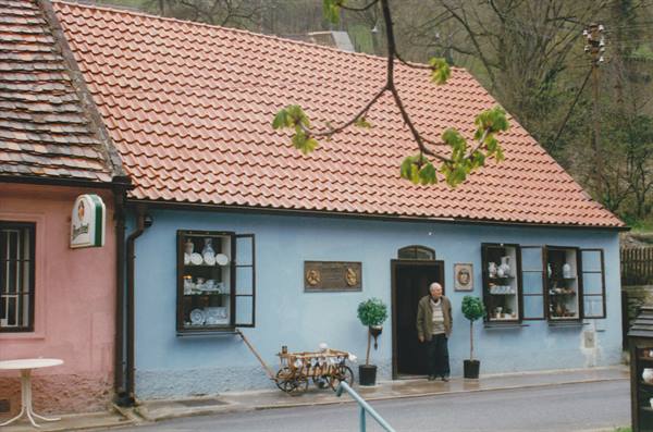 Elderly man at the door of a blue cottage with ceramics displayed in windows