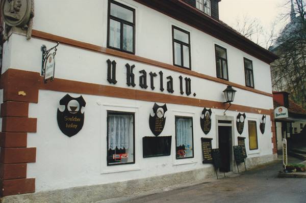 White pub facade with black shield-shaped signs reading 'U Karla IV'