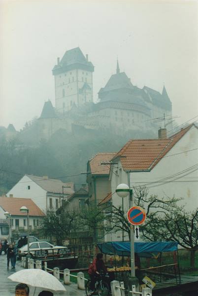 Karlštejn Castle in the fog above rooftops and the wet village street