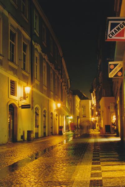 Cobbled street at night with exchange signs, glowing lamps and baroque buildings