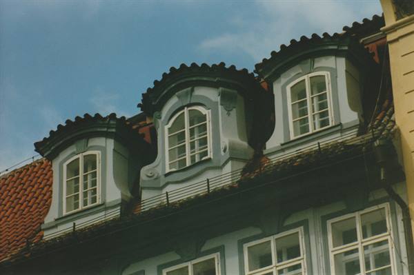 Three grey baroque dormer windows on red tile roof under blue sky
