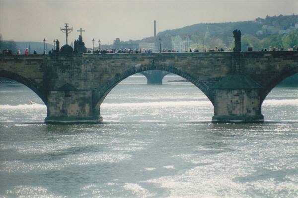 Charles Bridge stone statues over the Vltava, people walking, sunlight sparkling on water