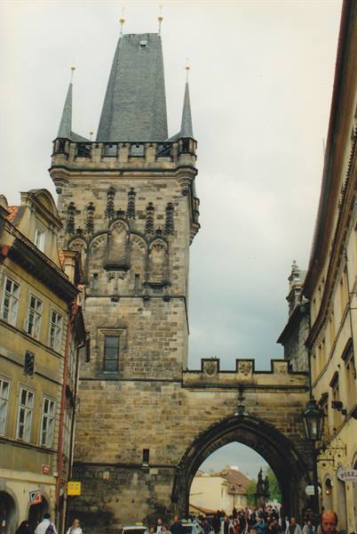 Tourists walk under the Gothic stone tower of Charles Bridge, Prague