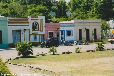 Vintage car and motorcycles parked before colorful colonial houses with palms