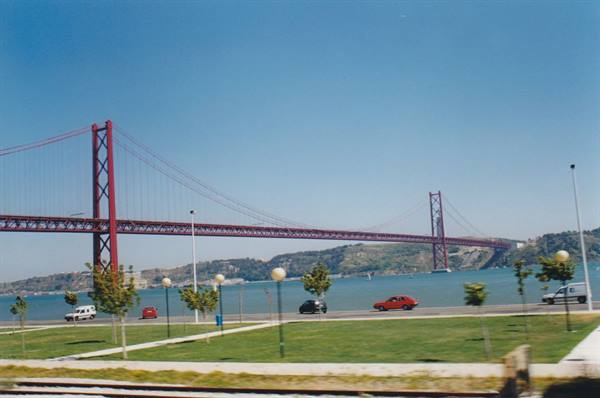 Red suspension bridge over the Tagus river with cars on the Lisbon waterfront road