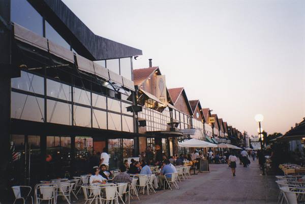 People seated at outdoor café tables in front of glass-walled warehouses at dusk