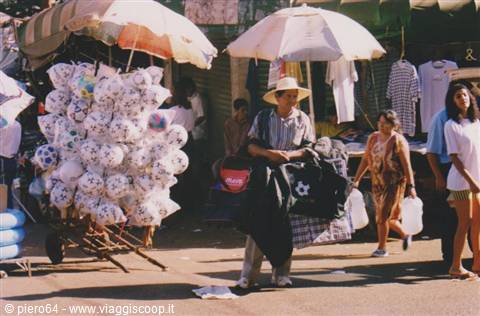 Straw-hatted vendor beside a cart of balloon bunches at the market