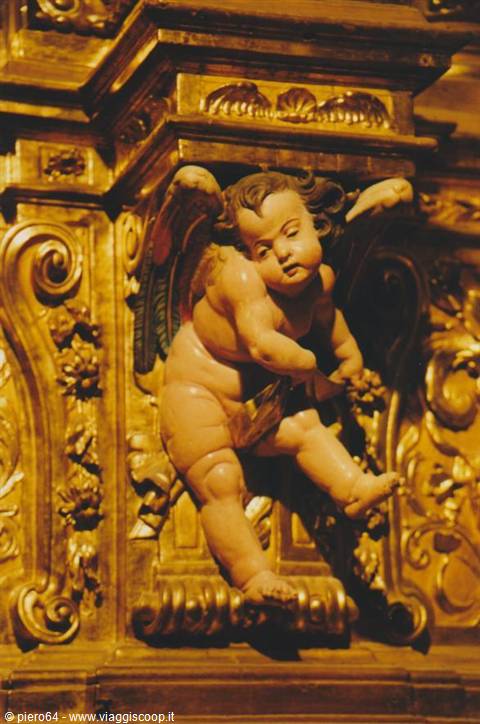Carved cherub angel on a gilded wooden altarpiece under warm light