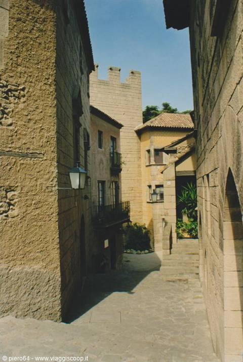 Steep alley between stone walls with crenellated tower, sunlight