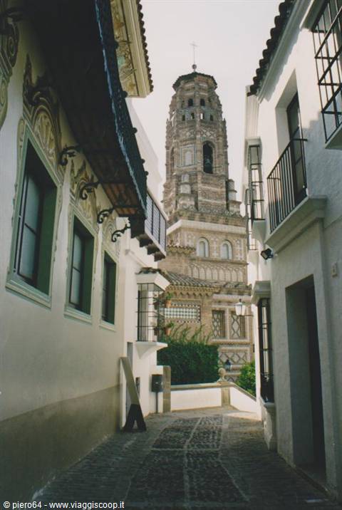Cobblestone alley with white houses toward the mudéjar tower in Écija
