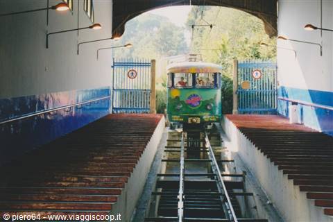 Green funicular car arriving on tracks between blue gates at the station