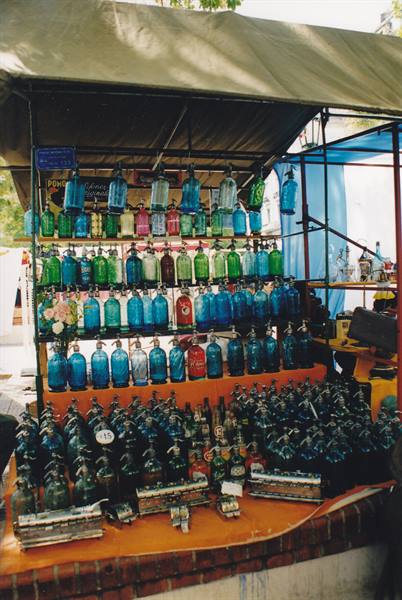 Market stall displaying colorful antique glass bottles and oil lamps for sale