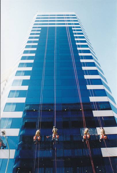Workers on ropes cleaning the blue glass facade of a skyscraper