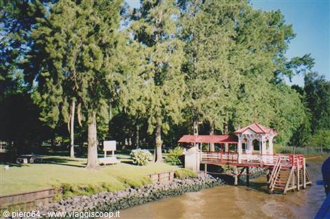 Red stilt kiosk along the river among tall trees and green lawn