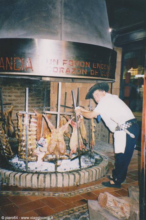Chef in hat rotates meat skewers over open fire grill inside restaurant