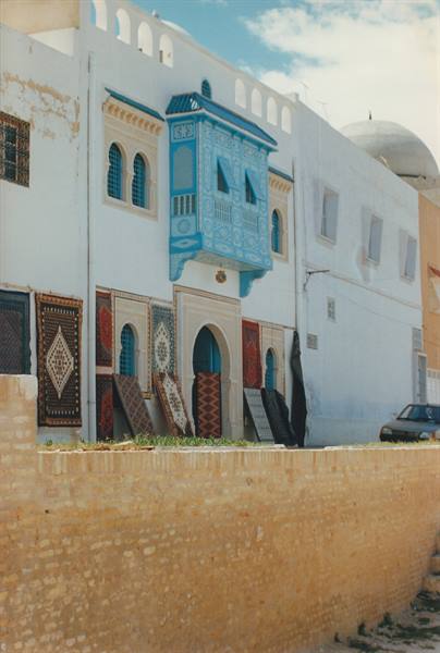 White house with blue wooden balcony and carpets hung outside