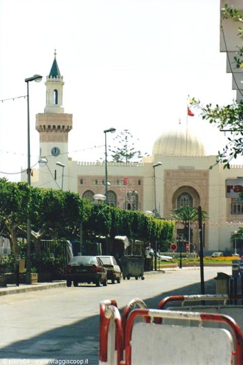 White-domed mosque with clock minaret, cars parked along the sunny street