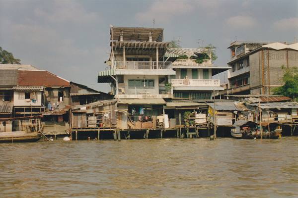 Wooden stilt houses along the muddy river, small boat moored nearby