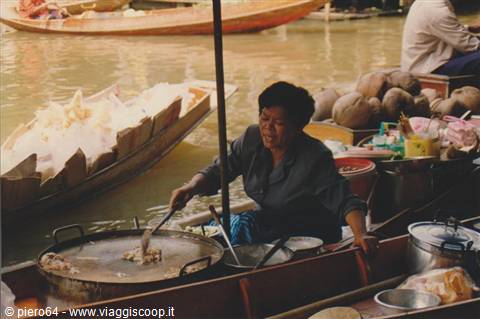 Woman cooking on a boat at floating market, wok and coconuts