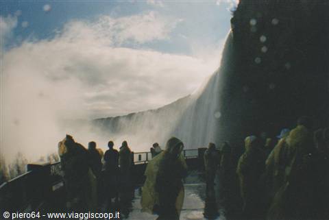 Visitors in yellow raincoats facing Niagara Falls, spray and mist rising