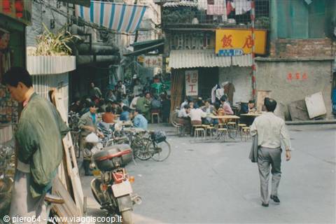 Men sitting at street food stall tables, bicycles and scooter parked, Chinese signs