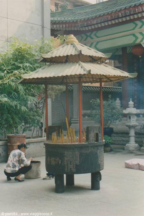 Woman crouching lights incense sticks in the large iron brazier, Chinese temple