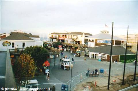 Visitors stroll the wooden plaza of Pier 39, Colorful signage, gray light