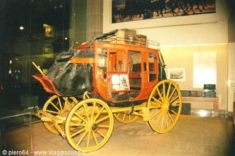 Orange stagecoach with yellow wheels displayed in museum under warm light