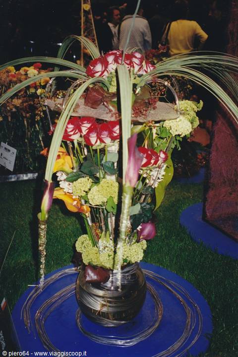 Floral arrangement with red roses and calla lilies in metal vase at exhibition