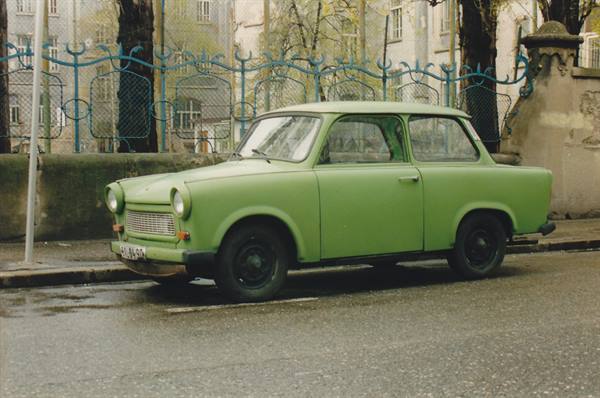 Green Trabant car parked at the curb in front of an iron fence