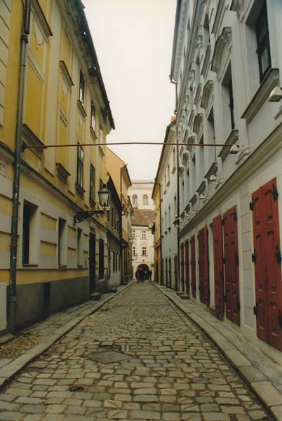 Cobblestone street between yellow and white buildings with red doors, old lamp