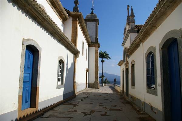 Baroque colonial church, white walls and blue doors, stone pavement, palm tree in sunlight