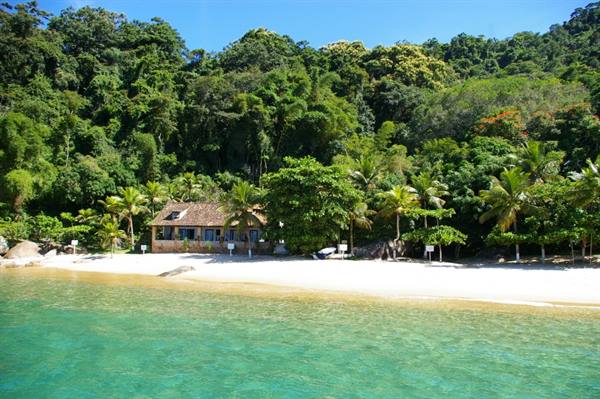 Wooden hut on sandy beach beneath tropical forest, turquoise water