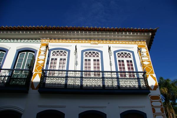 Colonial facade with wrought-iron balcony and yellow, blue ornaments against blue sky