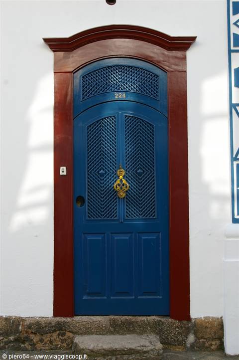 Blue wooden door with golden knocker, red frame on white wall