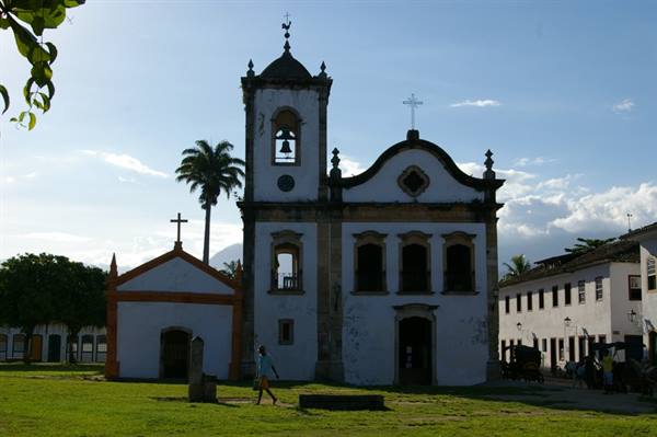 White colonial church with bell tower, cross and palm tree on green lawn