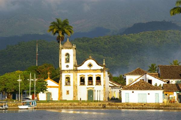 White colonial church with bell tower by the bay, moored boats, green hill