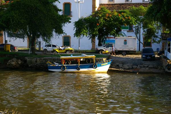Blue and yellow boat moored in front of white colonial buildings and trees