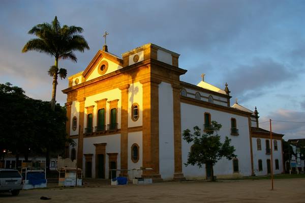 White colonial church with yellow stone corners, palm tree, golden light