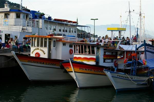 Painted boats moored at the pier with tourists and mountains behind