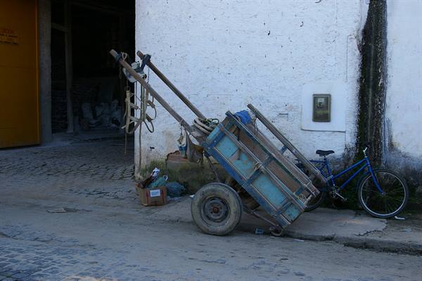 Tilted blue wooden cart beside a bicycle against a whitewashed wall