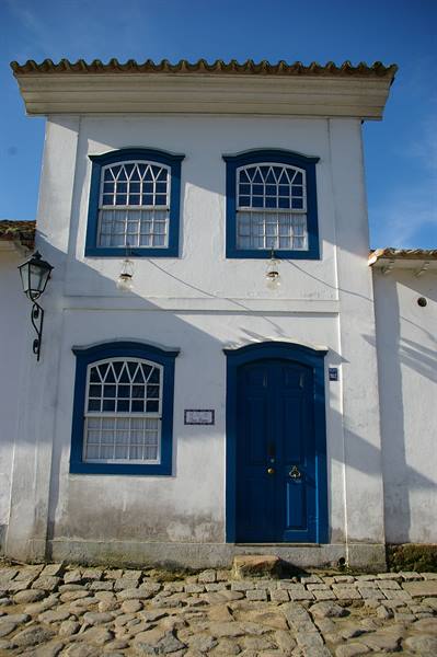 White colonial house with blue windows and door on cobblestones