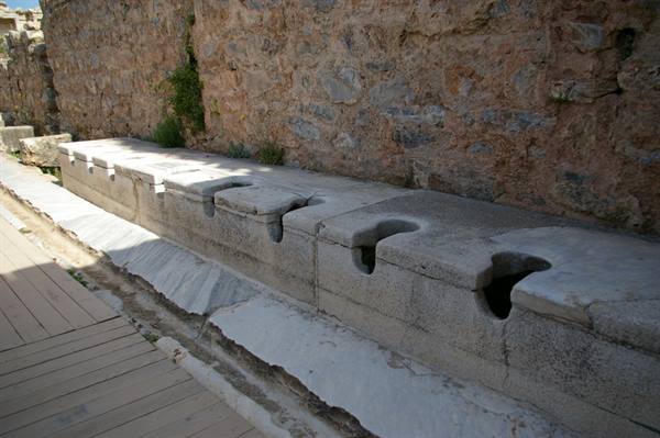 Ancient marble latrines along a stone wall, Ephesus