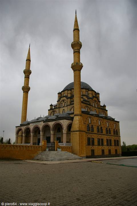 Yellow stone mosque with two minarets and dome under cloudy sky