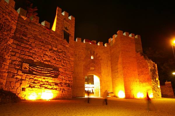 Stone fortress gate lit up at night, people passing under the archway