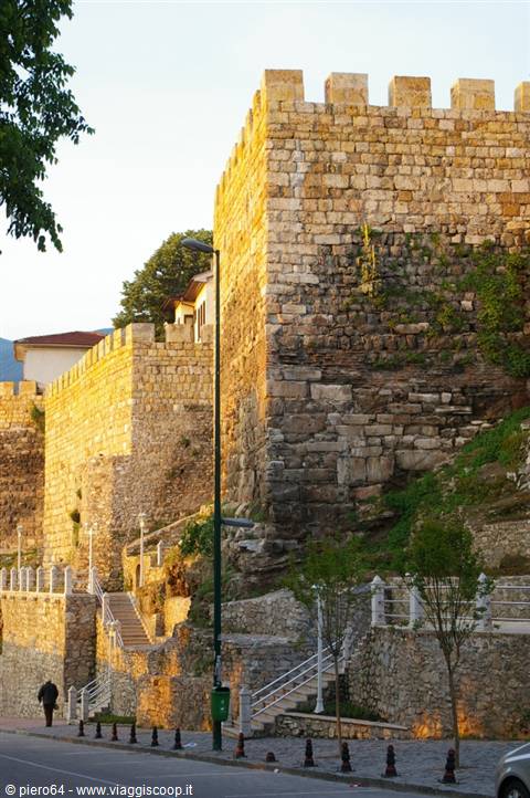 Ancient crenellated stone walls bathed in golden light, stairways and busy street