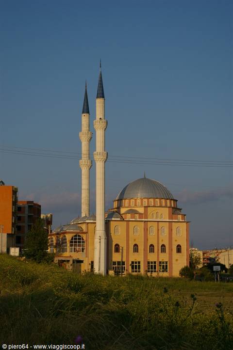 Yellow mosque with metal dome and two white minarets, evening light